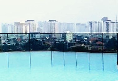 A distant city skyline seen across the still surface of a rooftop pool.